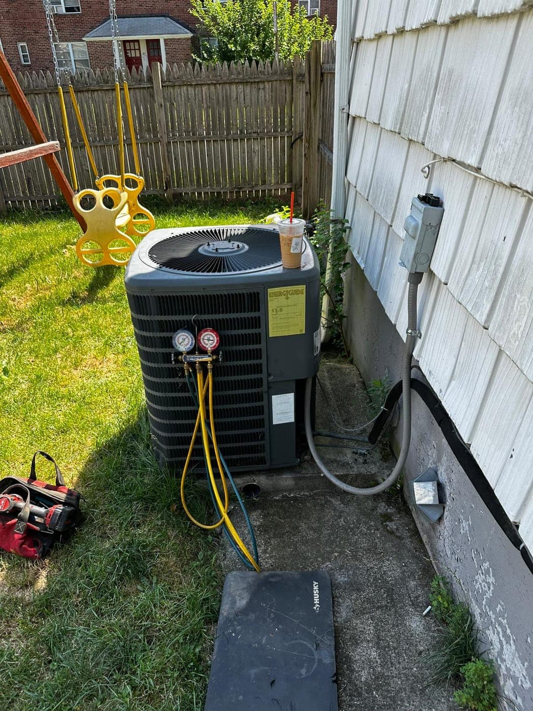 Technician servicing a residential air conditioning condenser beside a North Jersey home