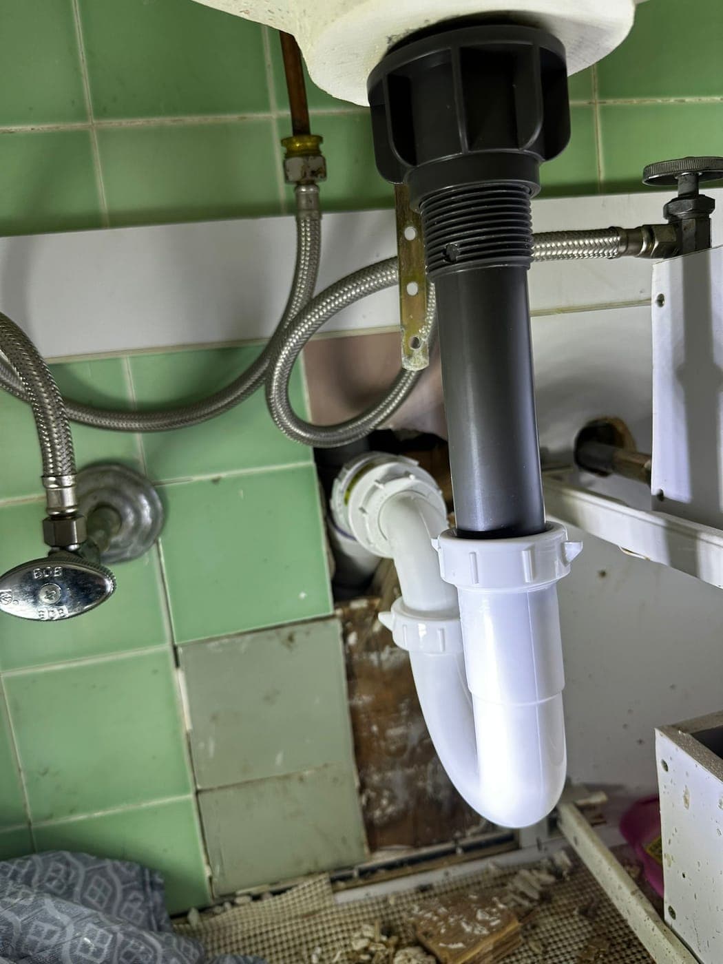 Kitchen sink drain trap and waste piping under a cabinet during a drain cleaning visit